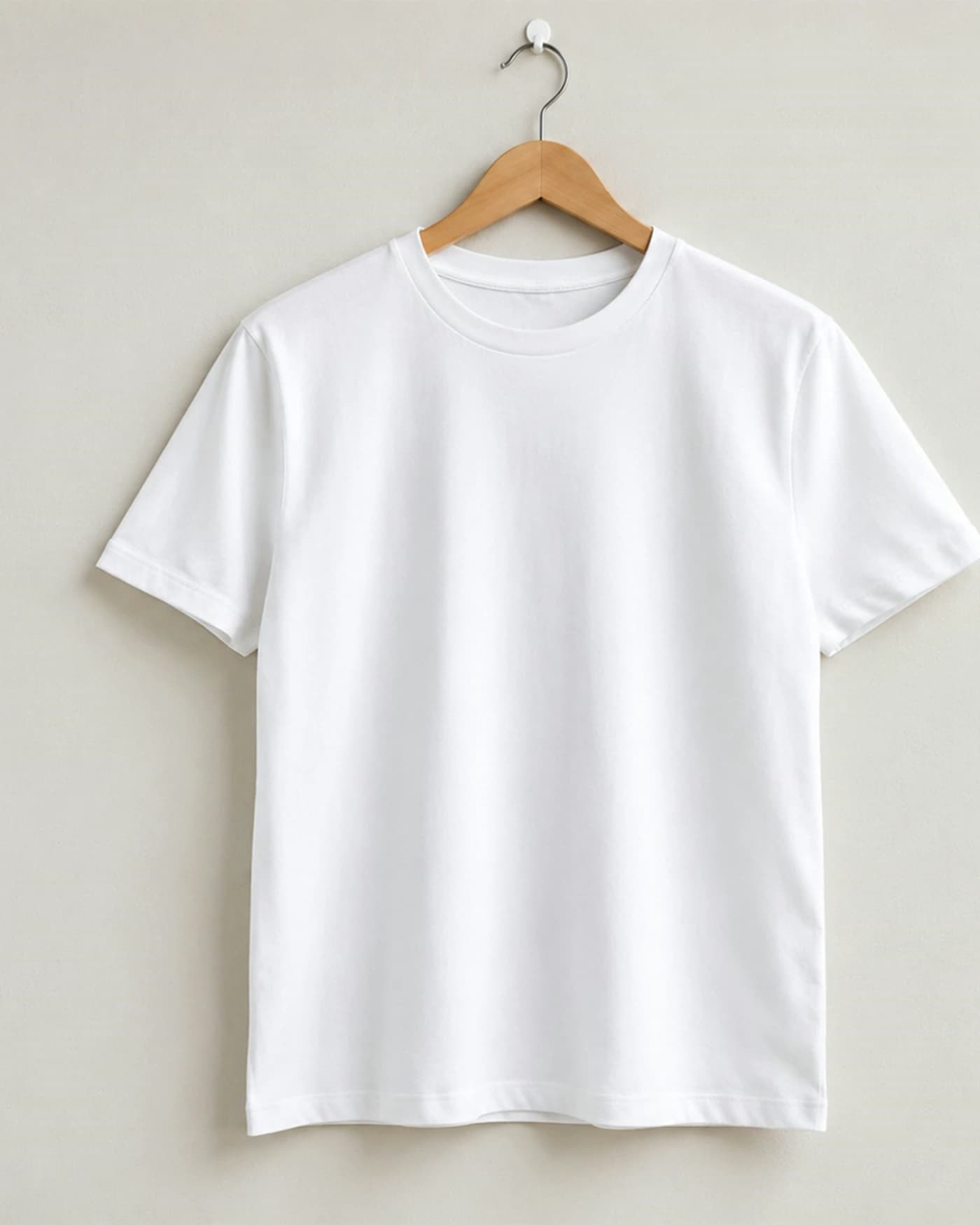 A plain white tee on a wooden hanger against a bare wall, entirely undecorated.