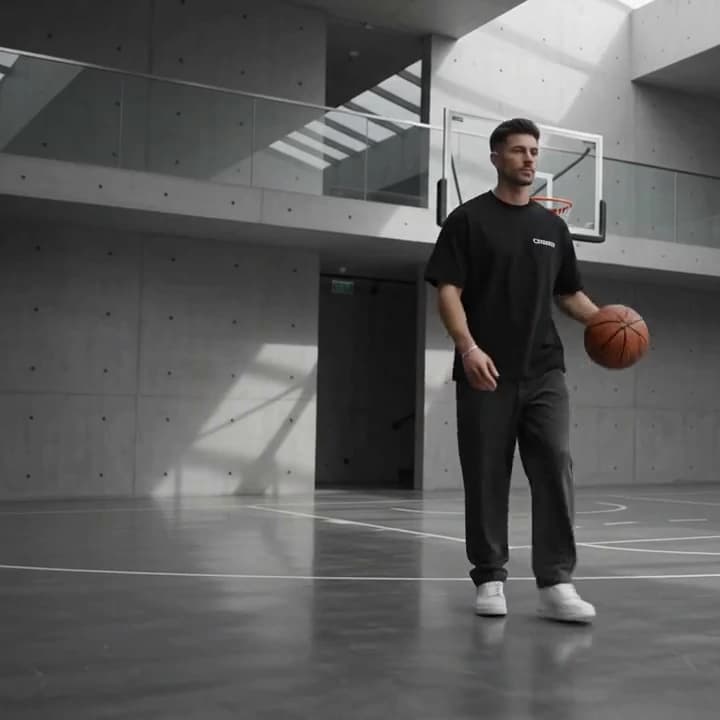 A man in a black CROOWDIO tee bouncing a basketball, alone on a wide concrete court.