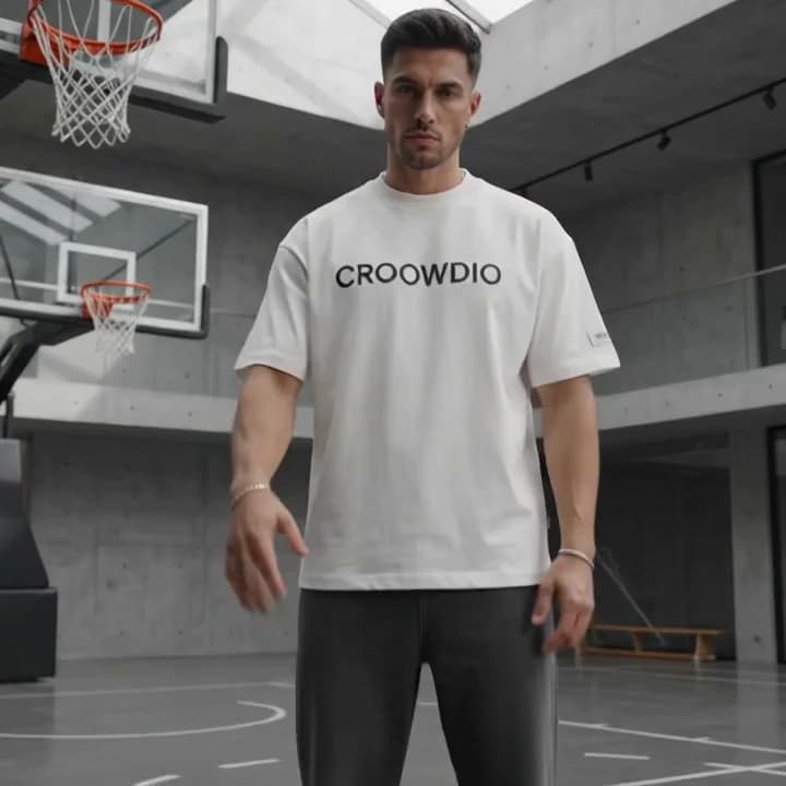 A man in a bone-white CROOWDIO tee standing square to camera on the empty court.