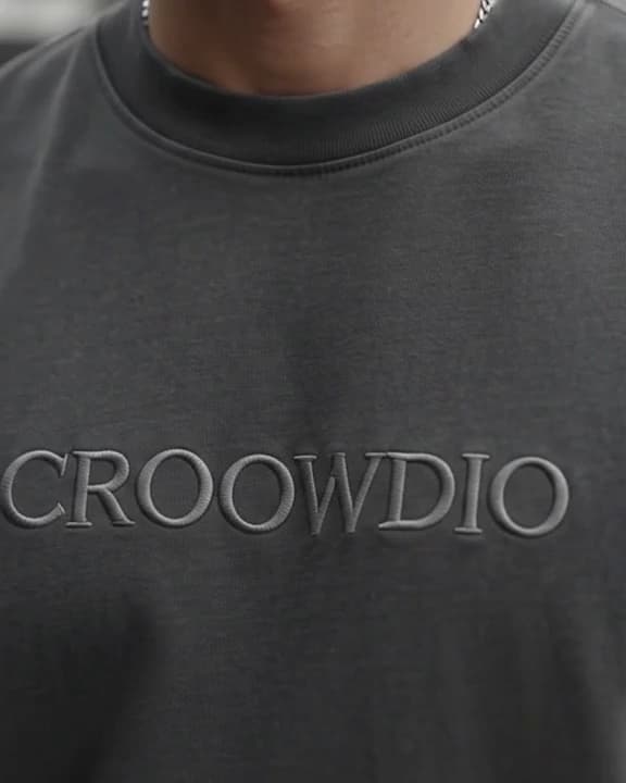 Close crop of a charcoal tee, CROOWDIO embroidered across the chest in thread the same colour as the cloth.