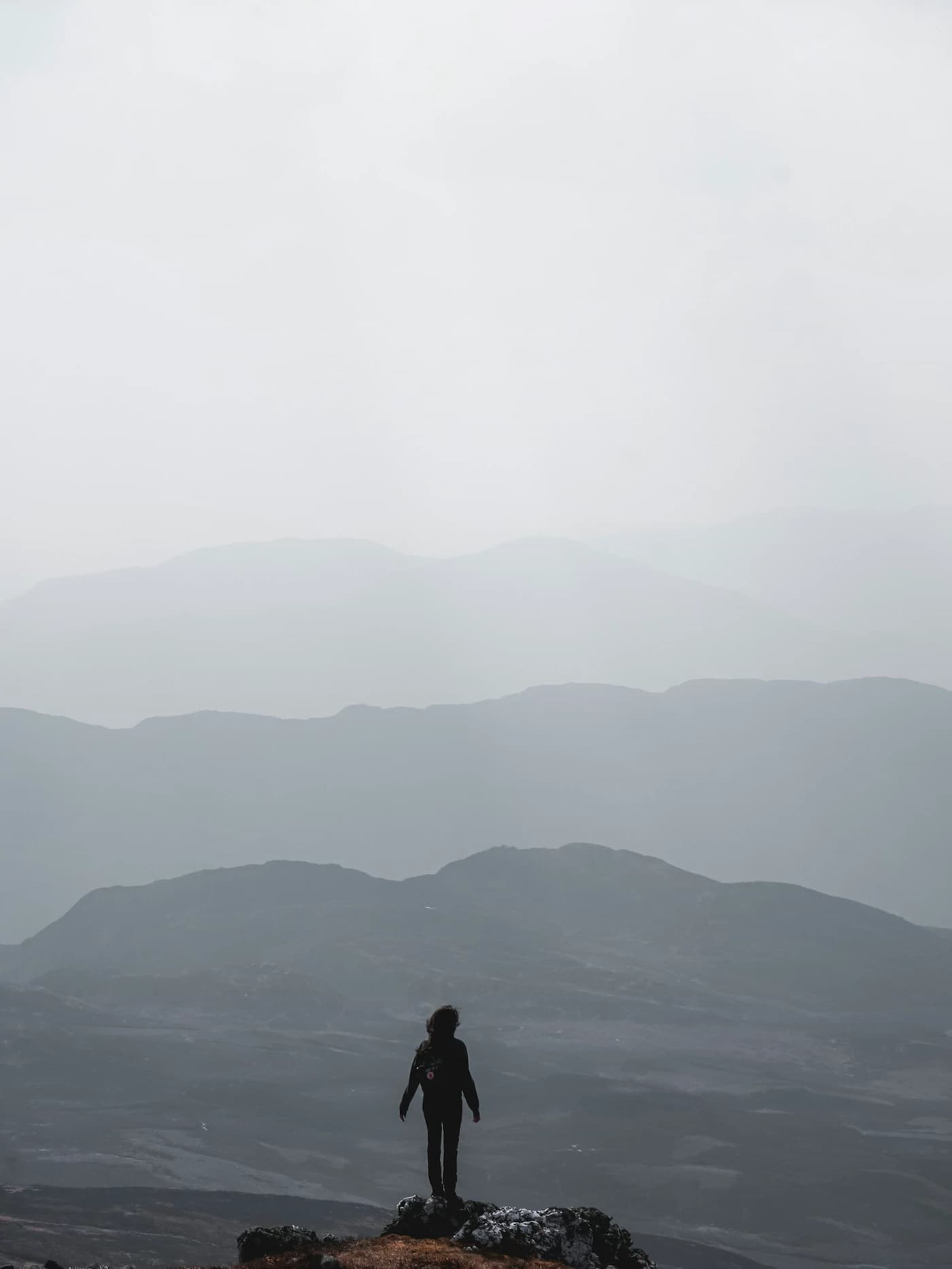 A lone figure on a ridge, looking out over range after range of mountains fading into haze.